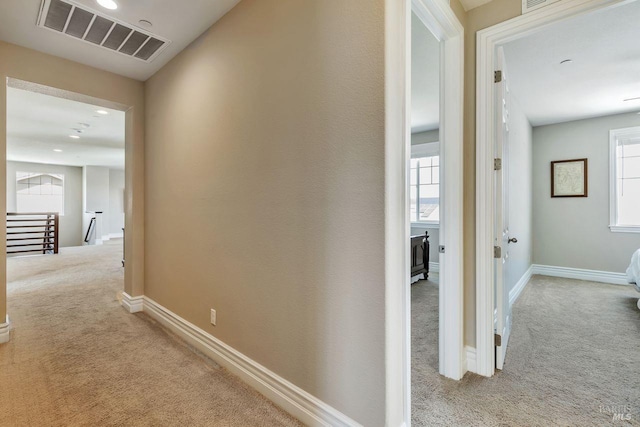 hallway with carpet flooring, visible vents, an upstairs landing, and baseboards