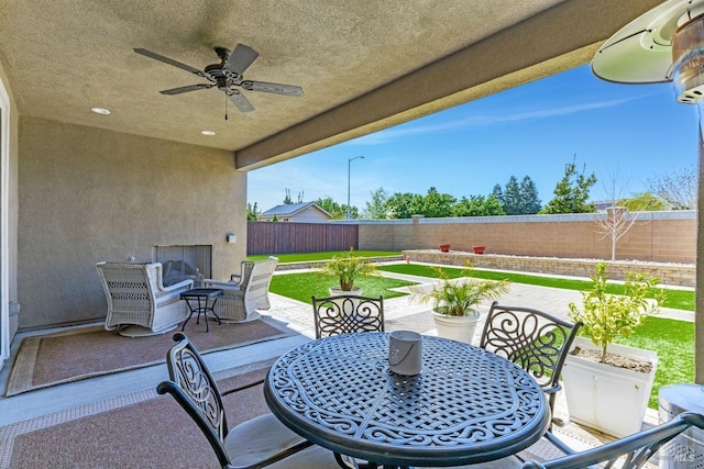 view of patio with a fenced backyard, ceiling fan, exterior fireplace, and outdoor dining area