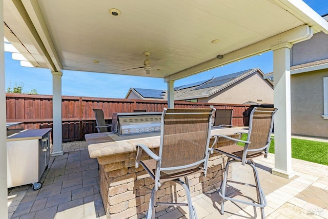 view of patio / terrace featuring ceiling fan, fence, outdoor wet bar, and an outdoor kitchen
