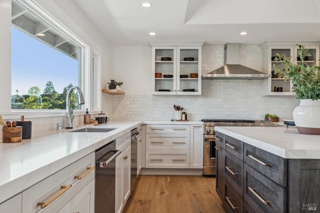 kitchen with wall chimney range hood, appliances with stainless steel finishes, white cabinetry, and a sink