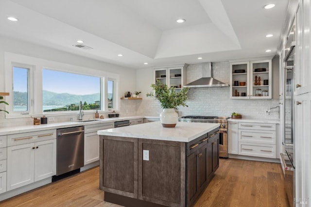 kitchen featuring wood finished floors, a sink, wall chimney exhaust hood, appliances with stainless steel finishes, and decorative backsplash