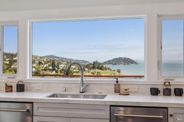 interior space featuring a sink, stainless steel dishwasher, light stone countertops, and decorative backsplash