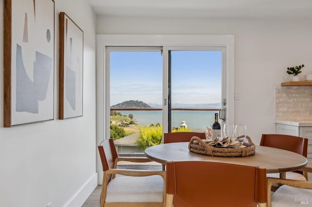 dining room with wood finished floors, a water view, and baseboards