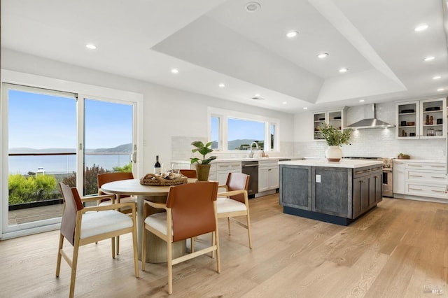 kitchen with stainless steel appliances, wall chimney exhaust hood, backsplash, a raised ceiling, and light countertops