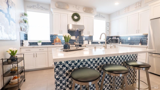 kitchen featuring freestanding refrigerator, tasteful backsplash, white cabinetry, and under cabinet range hood