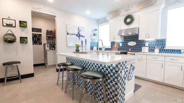 kitchen with tasteful backsplash, a sink, a breakfast bar, white cabinets, and under cabinet range hood