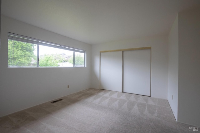 unfurnished bedroom with a closet, light colored carpet, and visible vents