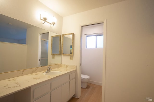 bathroom featuring toilet, vanity, wood finished floors, and baseboards