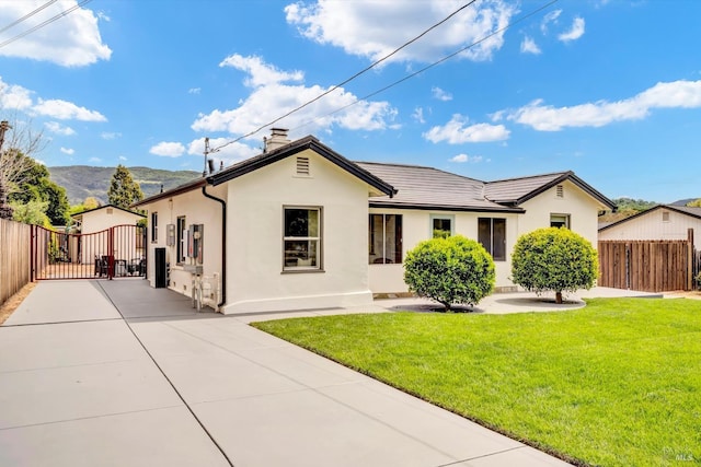 view of front of house featuring a gate, fence, a front lawn, stucco siding, and a mountain view