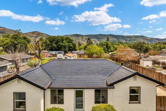 exterior space with stucco siding, solar panels, a mountain view, and fence