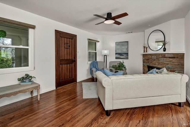 living room featuring visible vents, baseboards, a ceiling fan, wood finished floors, and a stone fireplace