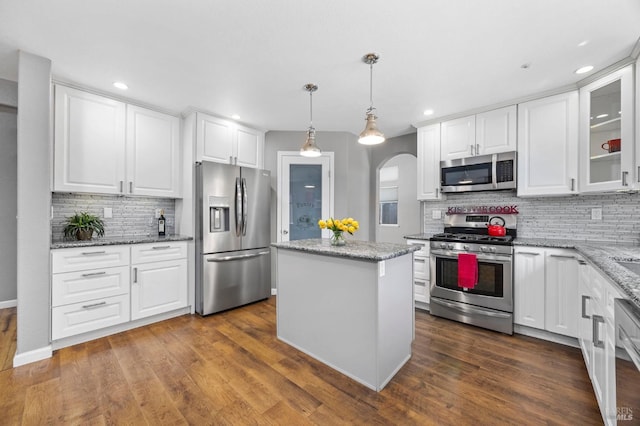 kitchen with tasteful backsplash, a kitchen island, white cabinets, appliances with stainless steel finishes, and arched walkways