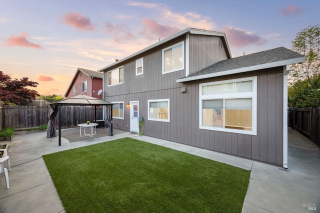 back of house at dusk with a patio, a yard, a fenced backyard, a gazebo, and a shingled roof