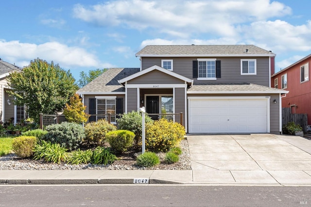 traditional-style home featuring an attached garage, a shingled roof, concrete driveway, and fence