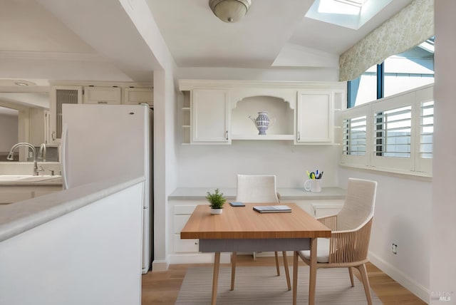 dining space featuring light wood-style floors, baseboards, and a skylight
