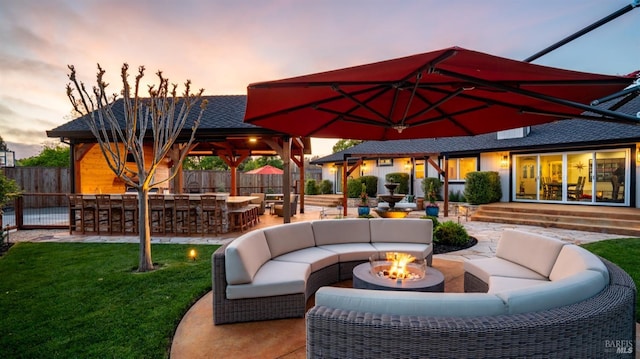 patio terrace at dusk featuring an outdoor living space with a fire pit, a gazebo, a lawn, fence, and a bar