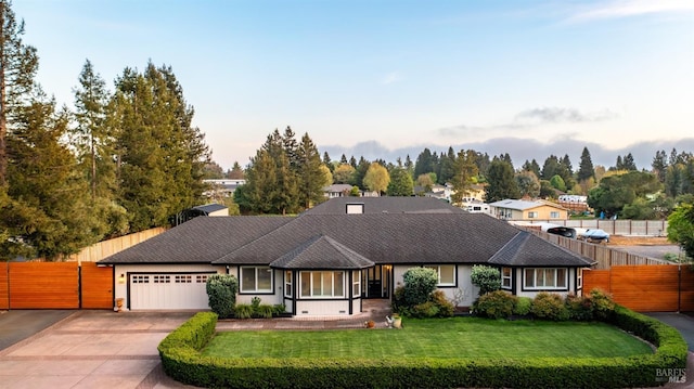 view of front facade featuring a front lawn, a shingled roof, driveway, an attached garage, and fence