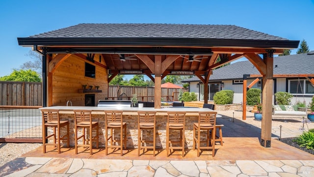 view of patio featuring a ceiling fan, a gazebo, exterior bar, and fence