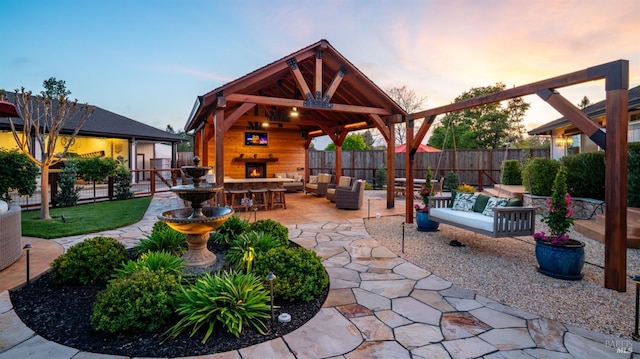 view of patio with fence, an outdoor living space with a fireplace, and a gazebo