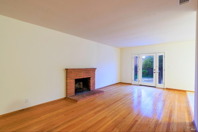 unfurnished living room with baseboards, light wood-type flooring, a fireplace, and visible vents