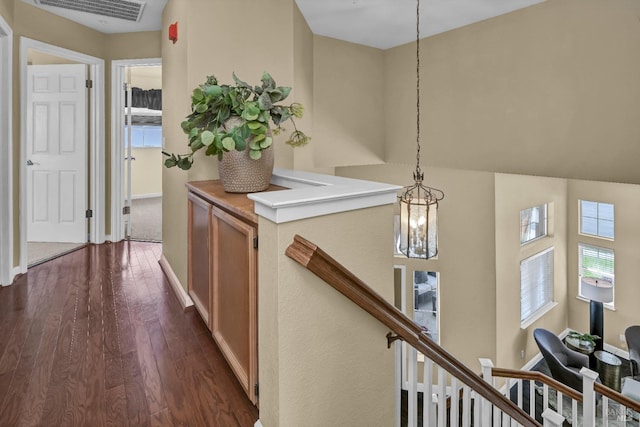 hallway with dark wood-type flooring, visible vents, baseboards, and an upstairs landing