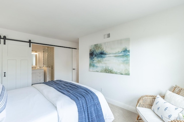 carpeted bedroom with visible vents, baseboards, ensuite bathroom, and a barn door