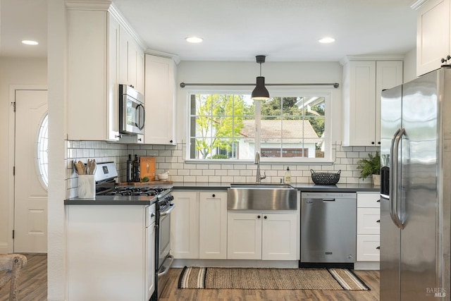 kitchen featuring dark countertops, white cabinets, appliances with stainless steel finishes, a sink, and wood finished floors