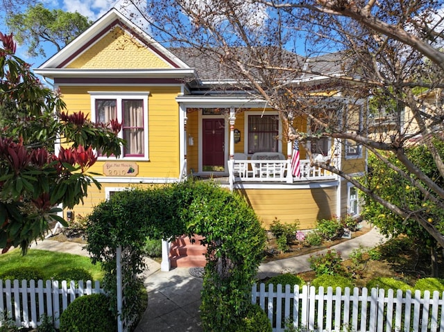 victorian house featuring a porch and a fenced front yard