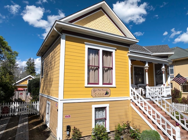 view of side of property featuring covered porch, fence, and stairway