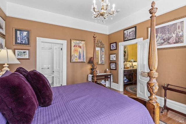 bedroom featuring ensuite bath, a notable chandelier, baseboards, and wood finished floors