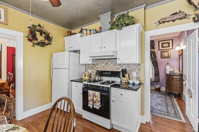 kitchen with tasteful backsplash, gas range oven, freestanding refrigerator, dark countertops, and under cabinet range hood