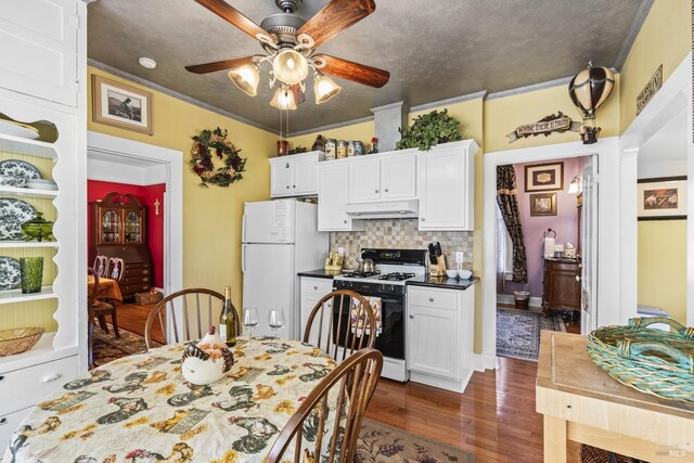 kitchen featuring ceiling fan, freestanding refrigerator, white cabinetry, under cabinet range hood, and gas stove