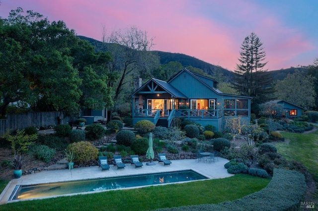 back of house at dusk featuring a lawn, fence, a patio, stairs, and an outdoor pool