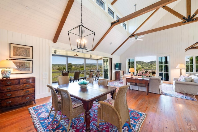 dining space featuring wood-type flooring, ceiling fan with notable chandelier, high vaulted ceiling, and beamed ceiling