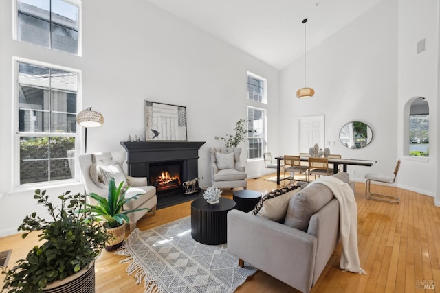 living area with a glass covered fireplace, baseboards, light wood-style floors, and high vaulted ceiling