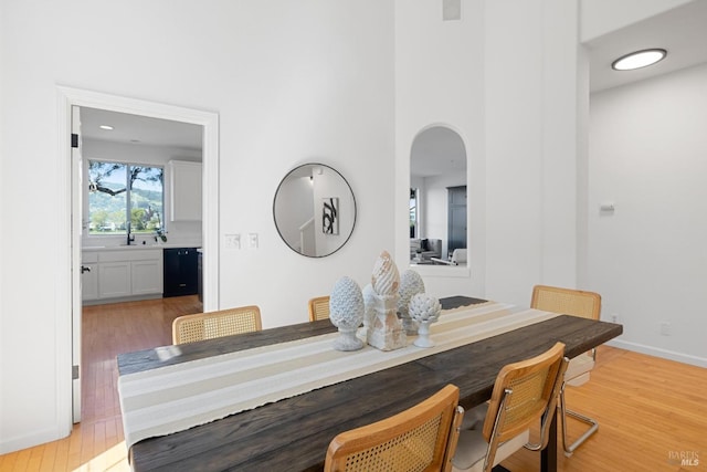dining room with light wood-type flooring, a high ceiling, baseboards, and arched walkways