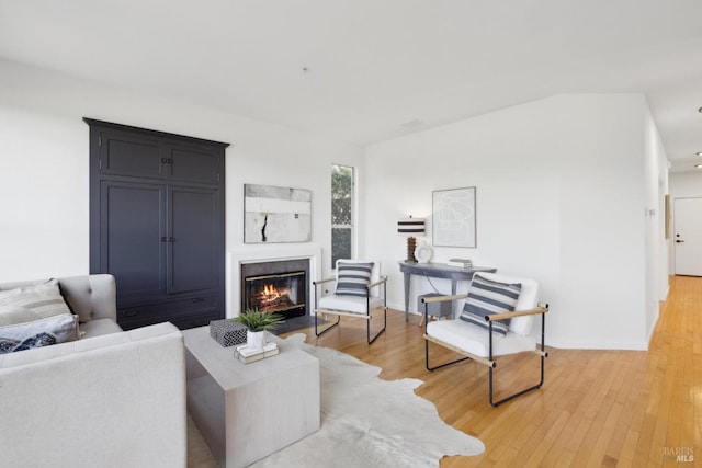 living room featuring a fireplace with flush hearth, baseboards, and light wood finished floors