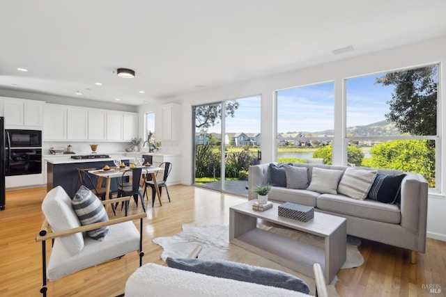 living area with light wood-style floors, a water view, and recessed lighting