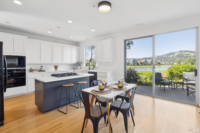 kitchen featuring light wood finished floors, white cabinets, a center island, light countertops, and black appliances