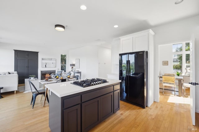 kitchen with light wood finished floors, open floor plan, white cabinetry, light countertops, and black appliances