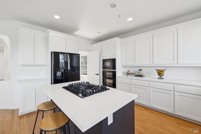 kitchen with light countertops, light wood-style floors, white cabinetry, a breakfast bar, and black appliances