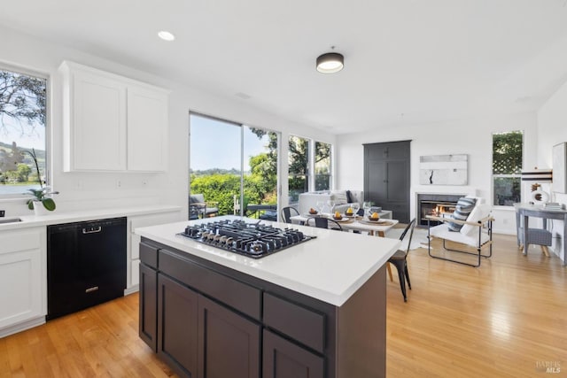 kitchen with light wood-style flooring, open floor plan, a glass covered fireplace, light countertops, and black appliances