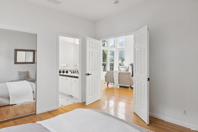 bedroom with light wood-style floors, ensuite bath, and baseboards