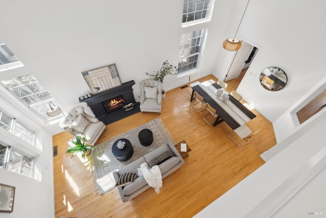 living area featuring a warm lit fireplace, wood finished floors, and a towering ceiling