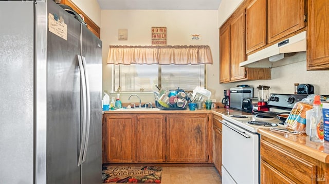 kitchen with light countertops, freestanding refrigerator, under cabinet range hood, brown cabinetry, and white electric range oven