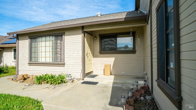 view of exterior entry with a patio and a shingled roof