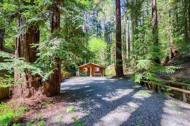 view of yard with an outdoor structure, a forest view, fence, and gravel driveway