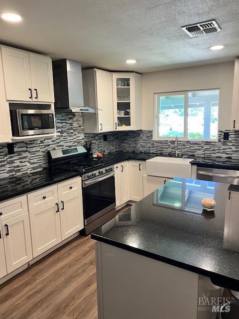 230 Lawrence St, Fairfield, CA 94533 - kitchen featuring appliances with stainless steel finishes, wall chimney range hood, a sink, white cabinetry, and wood finished floors
