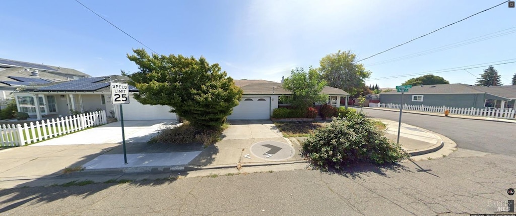 view of property hidden behind natural elements featuring a residential view, an attached garage, driveway, and fence