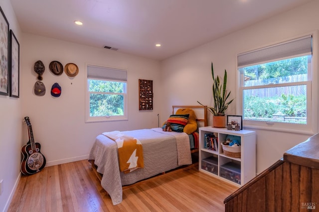 bedroom featuring light wood finished floors, baseboards, multiple windows, and visible vents